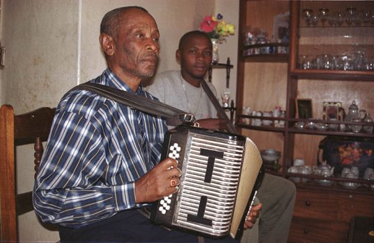 Kodé di Dona (2003), ou Gregório Vaz, na sua casa, em S. Francisco, arredores da Cidade da Praia. Ainda adolescente, nos anos 50 do século XX, teve a primeira gaita por troca com uma cabra. Na sua sabedoria, dizia que a vida de músico “é como uma vaca parida. Se tem bom tratamento dá muito leite, se não tem não dá nada. Também um homem, se toca um instrumento com fome, a música não é 'sabe'”.